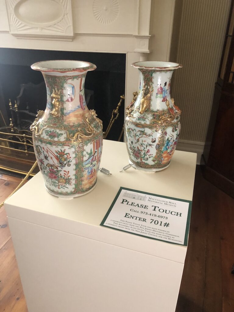 Porcelain vases are mounted on a pedestal. A label with directions for accessing an audio tour is visible to the right on the pedestal.